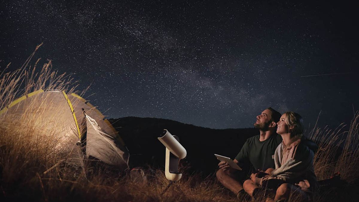 A man stargazing beside a telescope under a starry night sky.